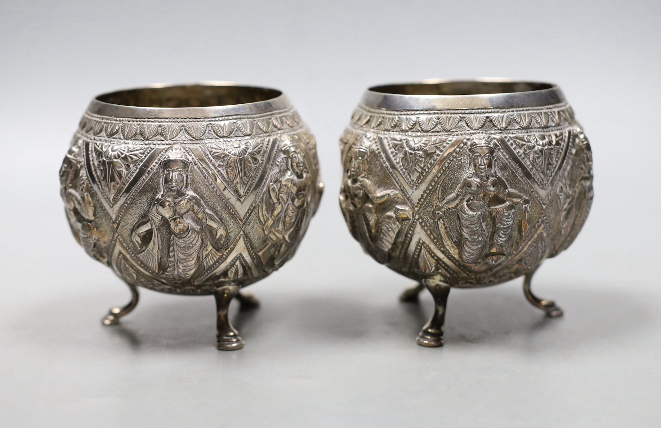 A pair of Indian embossed white metal circular bowls, on three hoof feet, height 82mm.